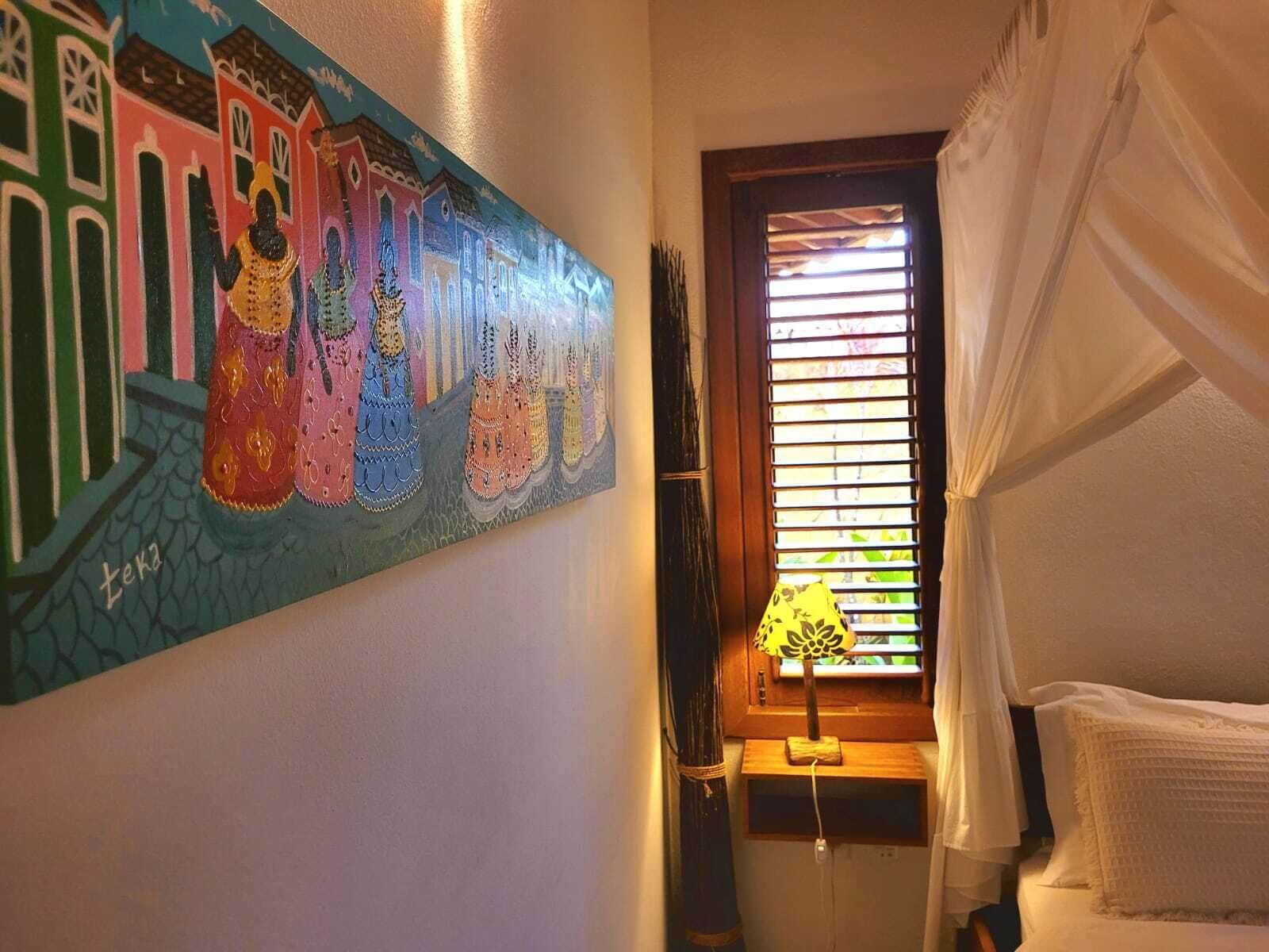 A room with a bed, a window with blinds, a lamp, and a wall painting.