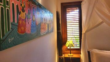 A room with a bed, a window with blinds, a lamp, and a wall painting.