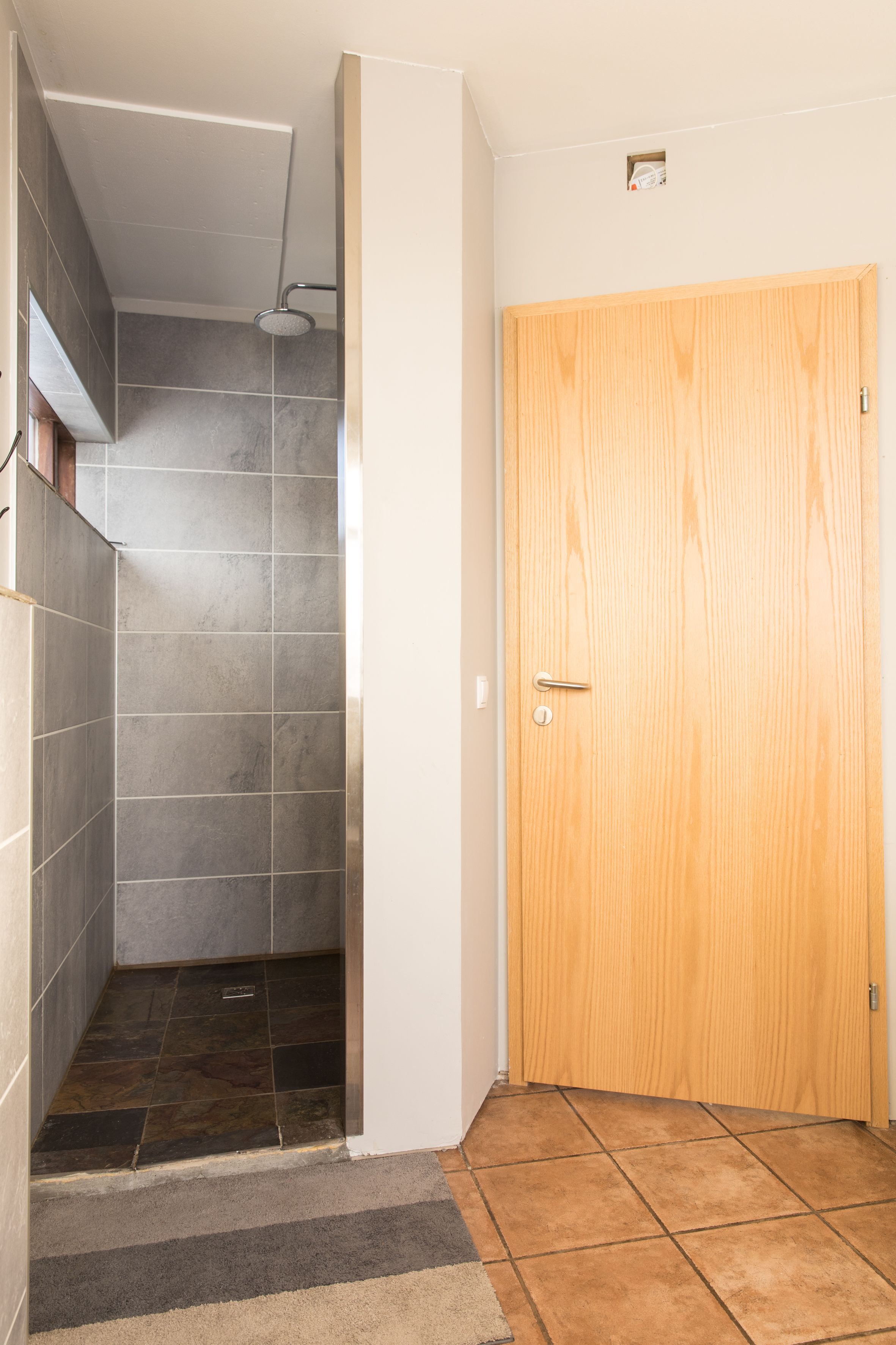 Un baño con ducha, paredes de azulejos, una puerta de madera y suelo de cerámica.
