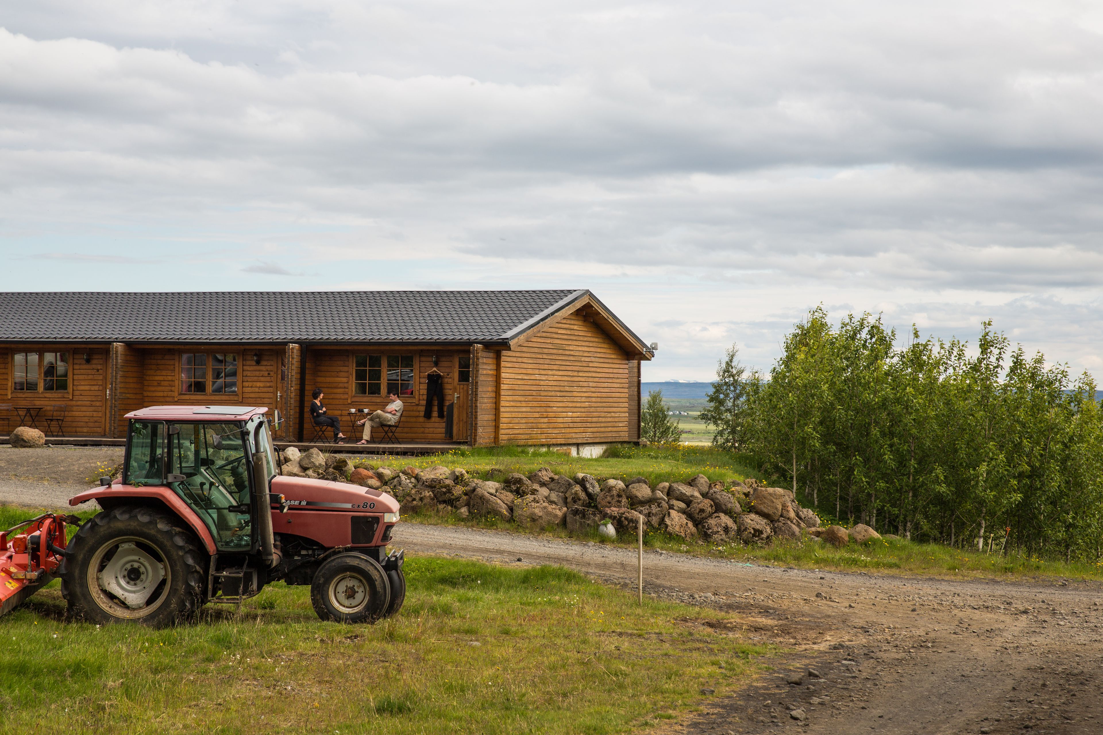 A wooden cabin with a porch, a red tractor in front, and a stone wall.