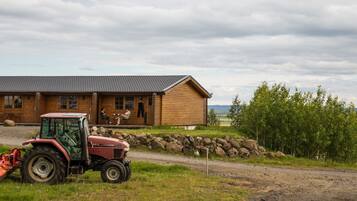 A wooden cabin with a porch, a red tractor in front, and a stone wall.