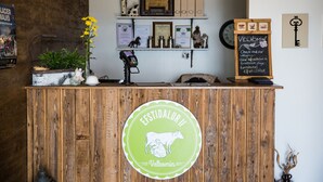 A wooden reception desk with a logo, a cash register, a plant, and various awards and certificates on the wall behind.