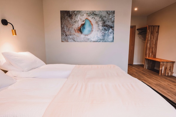 A bedroom with a large bed, a wall-mounted artwork, a wooden bench, and a hanging light fixture. - Farmhotel Efstidalur (Bláskógabyggd)