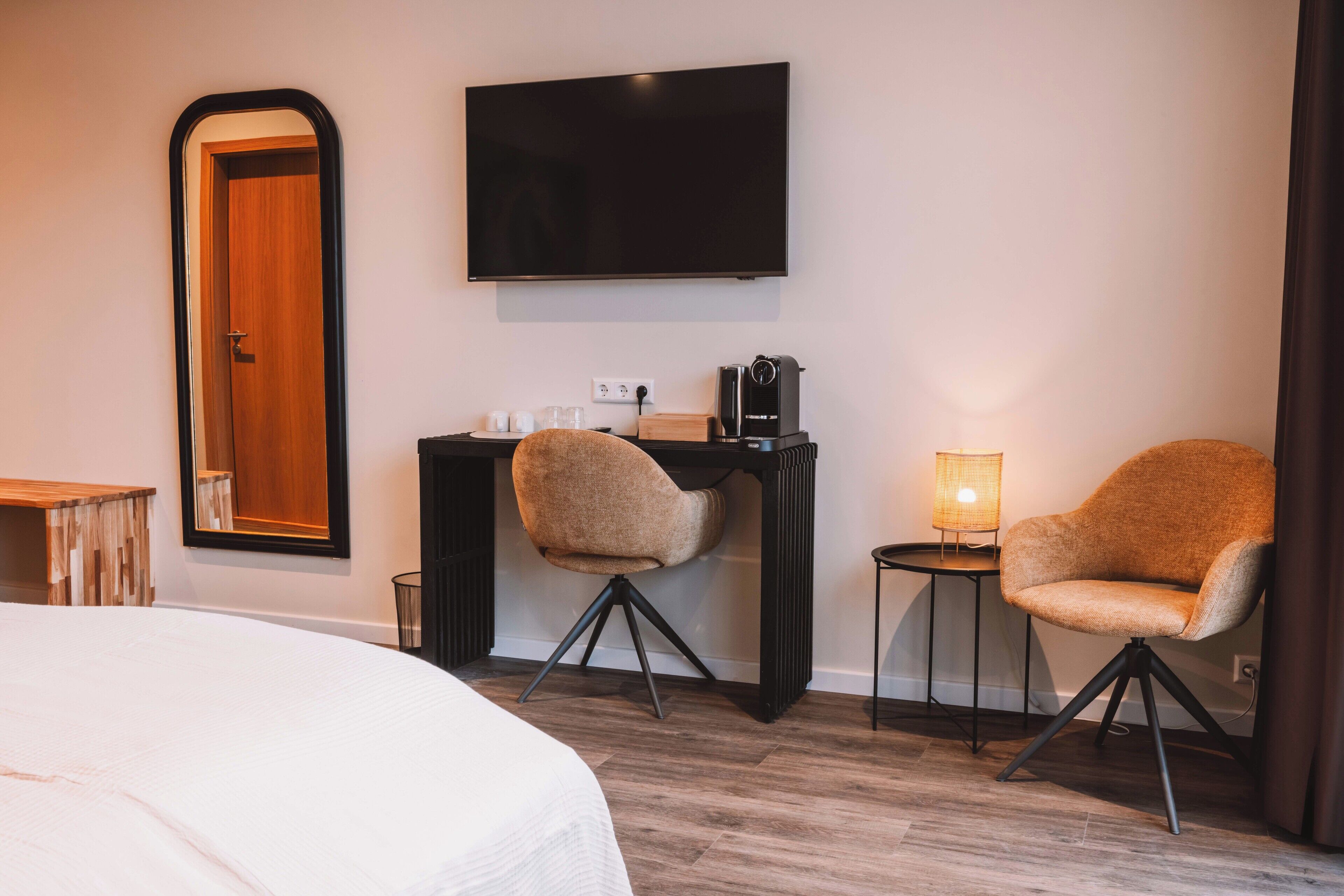 A hotel room with a bed, a desk, two armchairs, a TV, and a lamp.