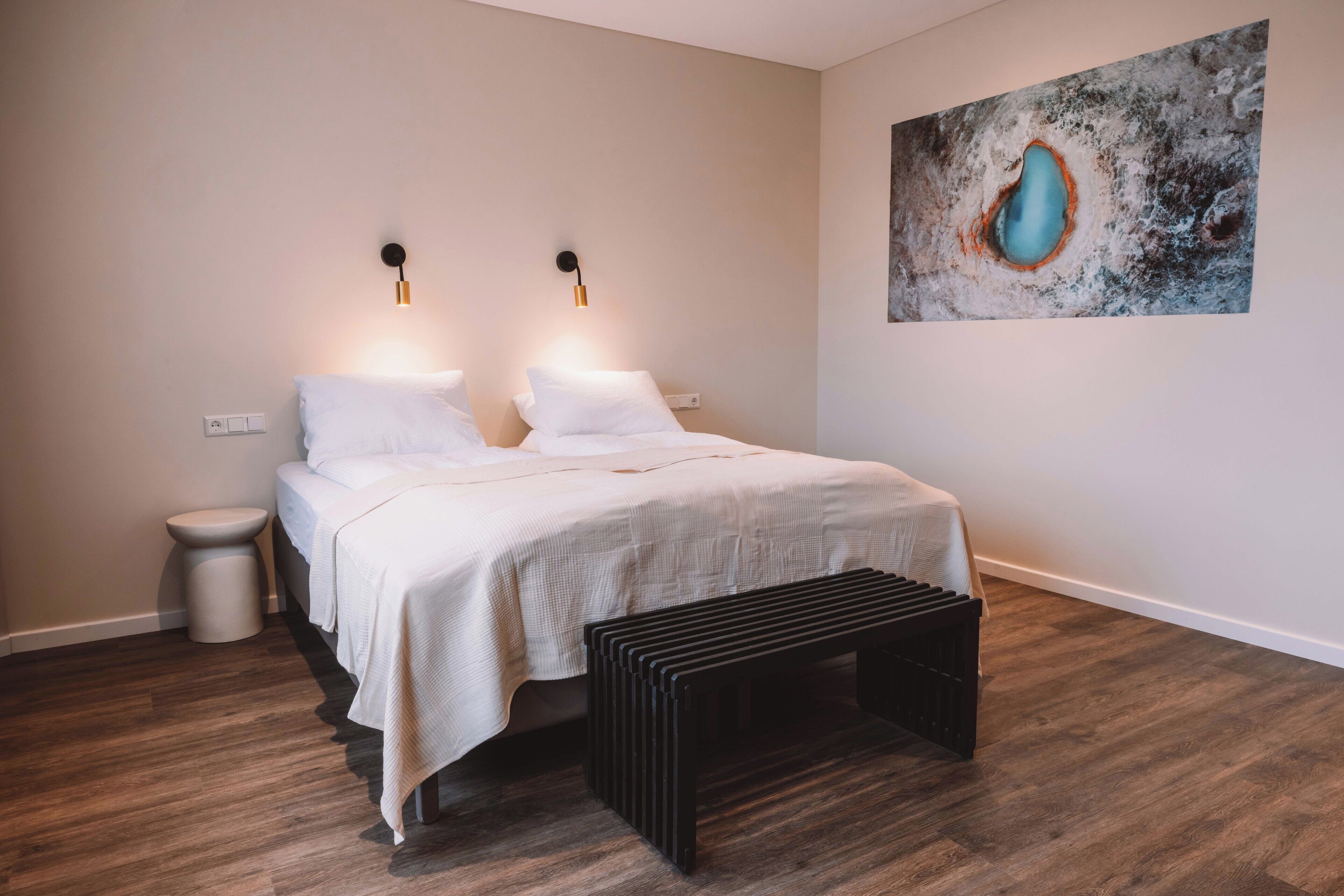 A bedroom with a bed, bedside lamps, a small stool, and a bench.