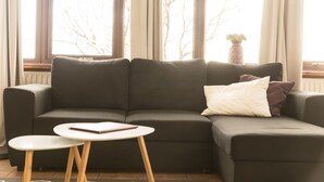 A modern living room with a dark grey sectional sofa, a small round table, and a potted plant on a windowsill.