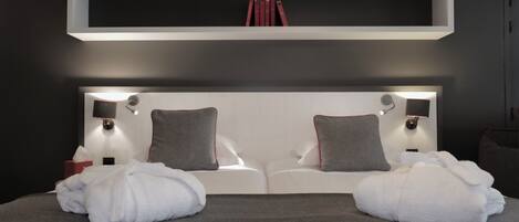 A modern hotel room with a large bed, two bedside tables, a headboard with integrated lighting, and a shelf above the bed.