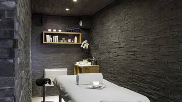 A modern spa room with a massage table, a shelf with toiletries, and a potted plant.