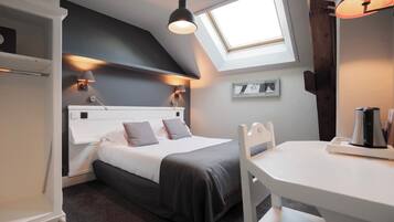 A bedroom with a bed, bedside lamps, a skylight, a white table, and a chair.