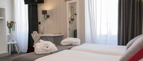 A hotel room with two beds, a TV, a mirror, a desk with a phone, and a vase with flowers.