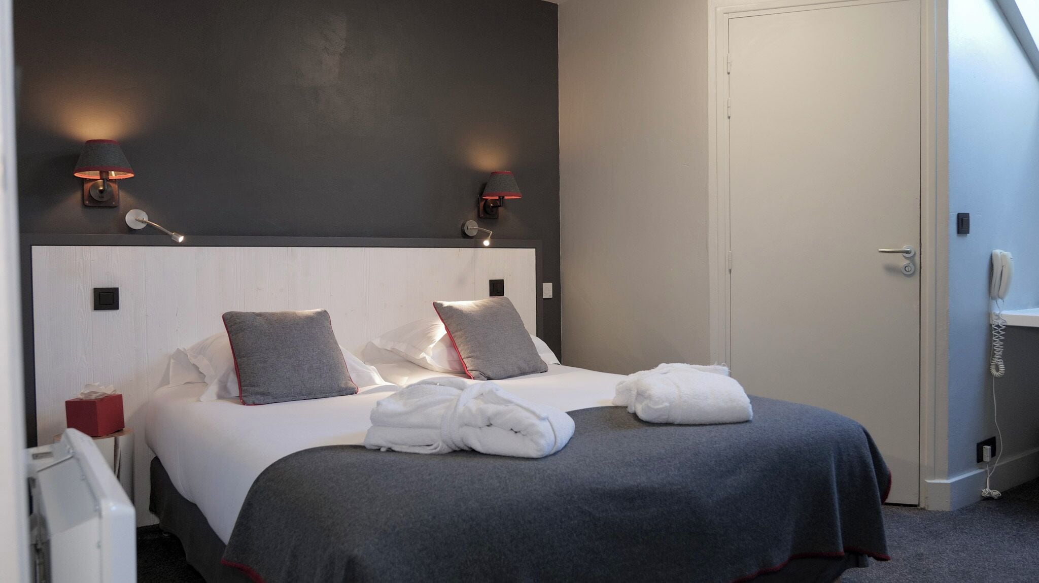 Ein Hotelzimmer mit einem großen Bett, zwei Nachttischlampen, einem Telefon und einer Tür.