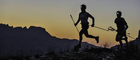 Two people running on a mountain trail with a sunset in the background.