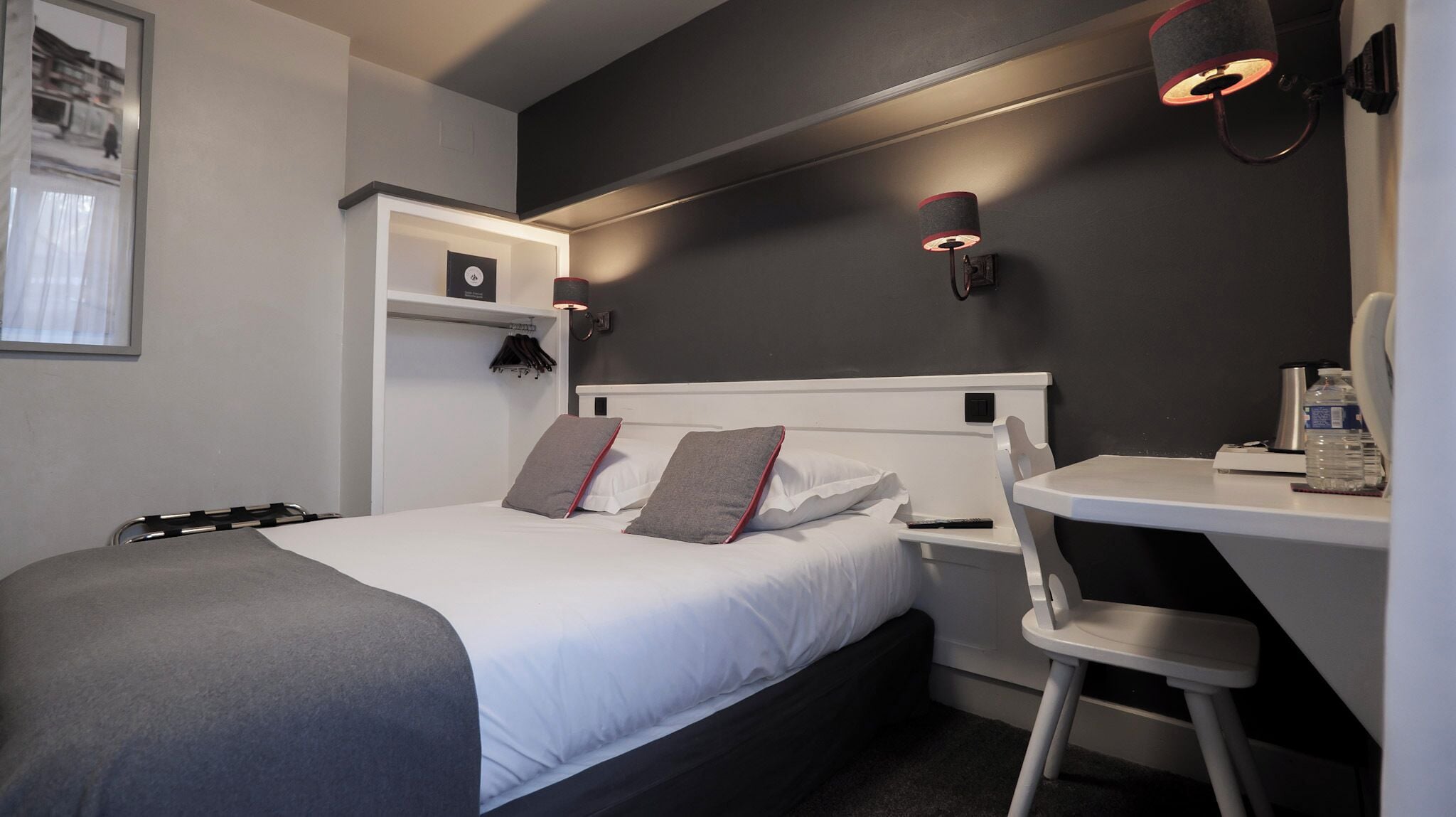 A modern hotel room with a bed, bedside table, chair, and a desk with a chair.