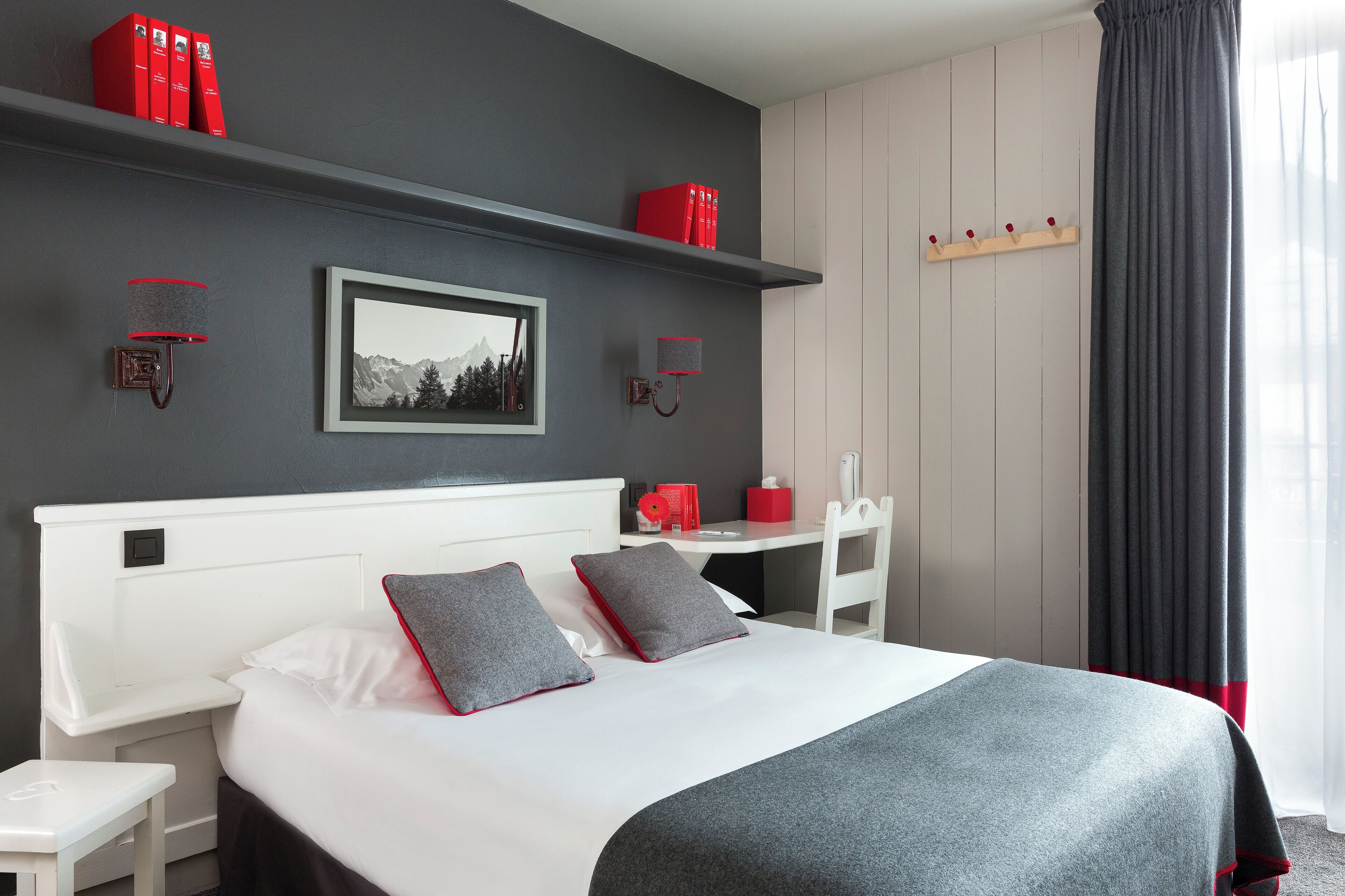 A modern hotel room with a large bed, a bedside table, a desk, and a wardrobe.