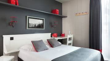 Ein modernes Hotelzimmer mit einem großen Bett, einem Nachttisch, einem Schreibtisch und einem Kleiderschrank.