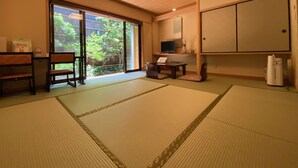 Een traditionele Japanse kamer met tatami vloeren, een schuifdeur naar een tuin, een televisie en een kast.