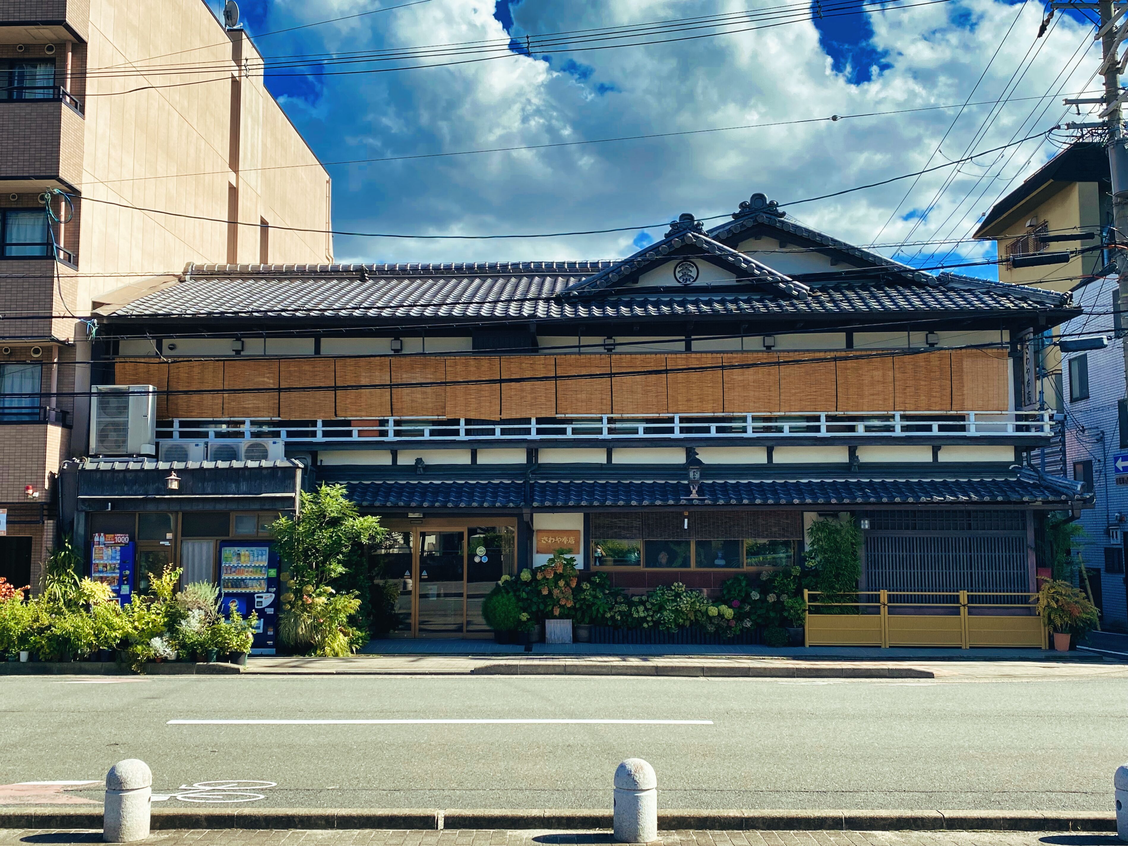 A traditional Japanese building with a tiled roof, a wooden facade, and a small garden area with potted plants.