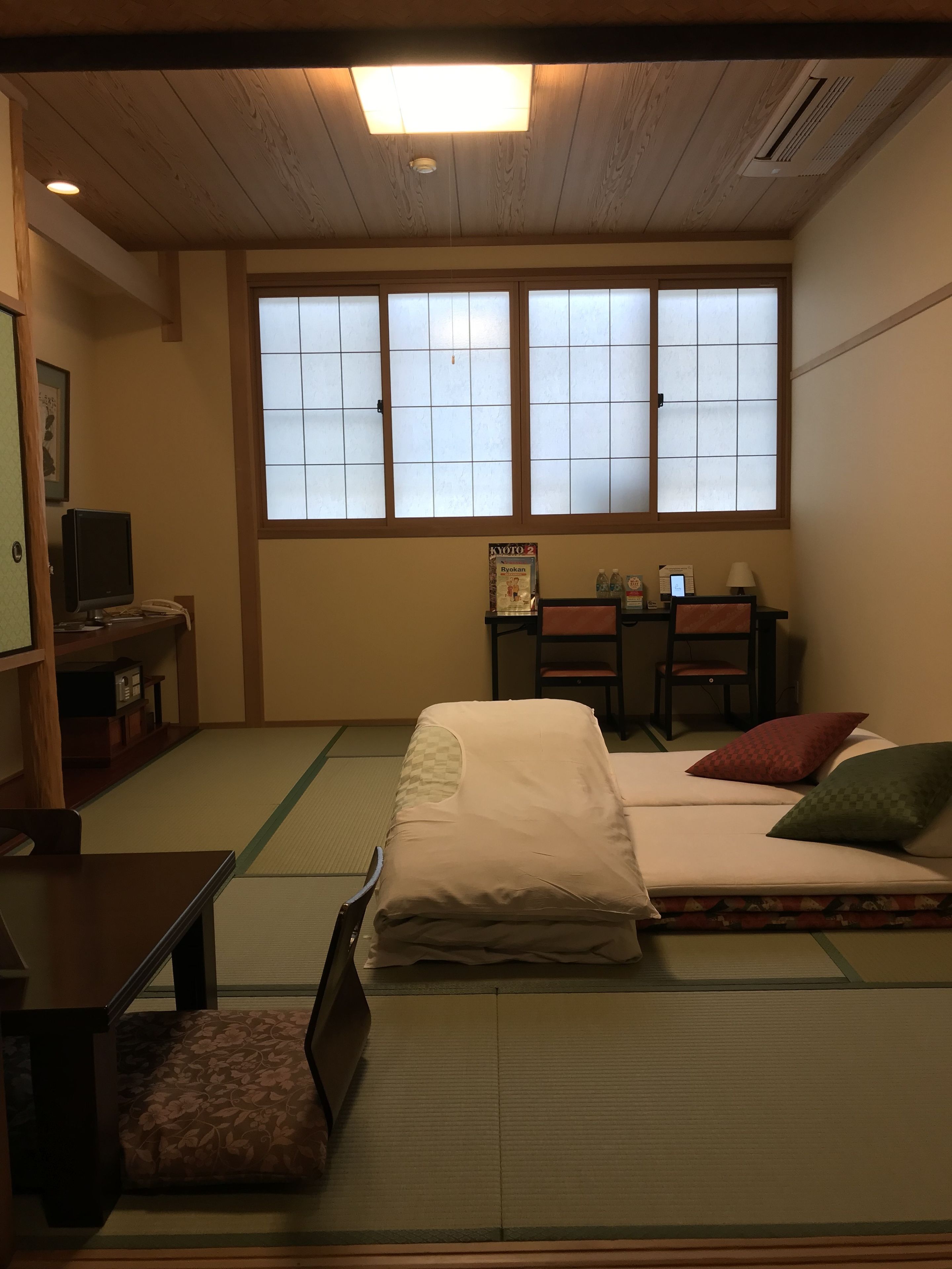 A traditional Japanese-style room with tatami flooring, a futon bed, a desk with a computer, and a window with shoji screens.