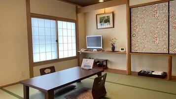 Una habitación tradicional japonesa con suelo de tatami, un escritorio de madera bajo, una computadora y un biombo decorativo.