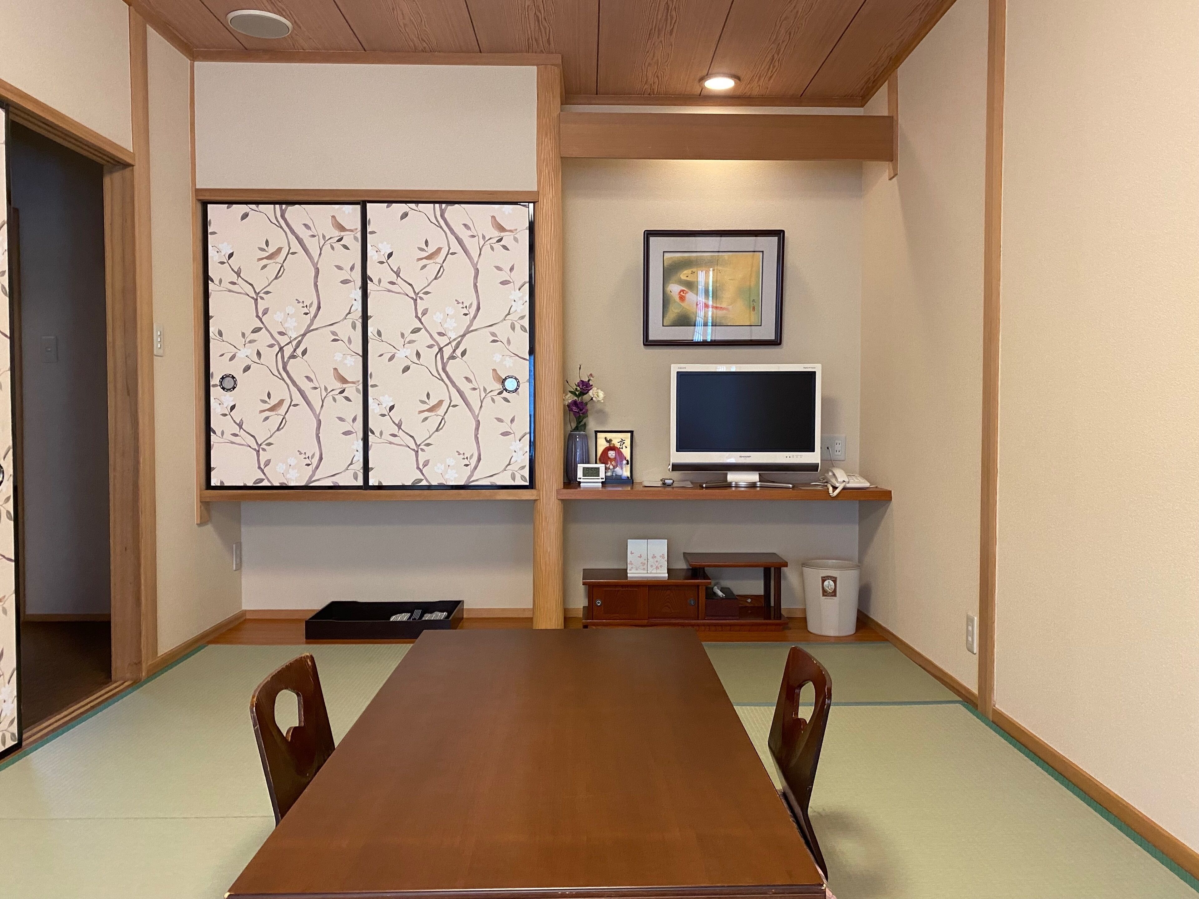 A traditional Japanese-style room with tatami flooring, a wooden table, and a television on a wooden stand.