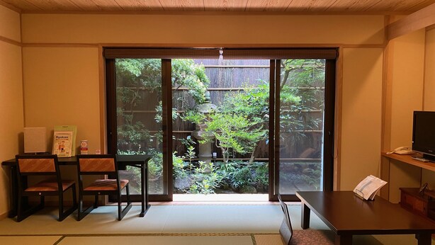 Een traditionele Japanse kamer met tatami vloeren, een schuifdeur naar een tuin, een lage tafel en een televisie.