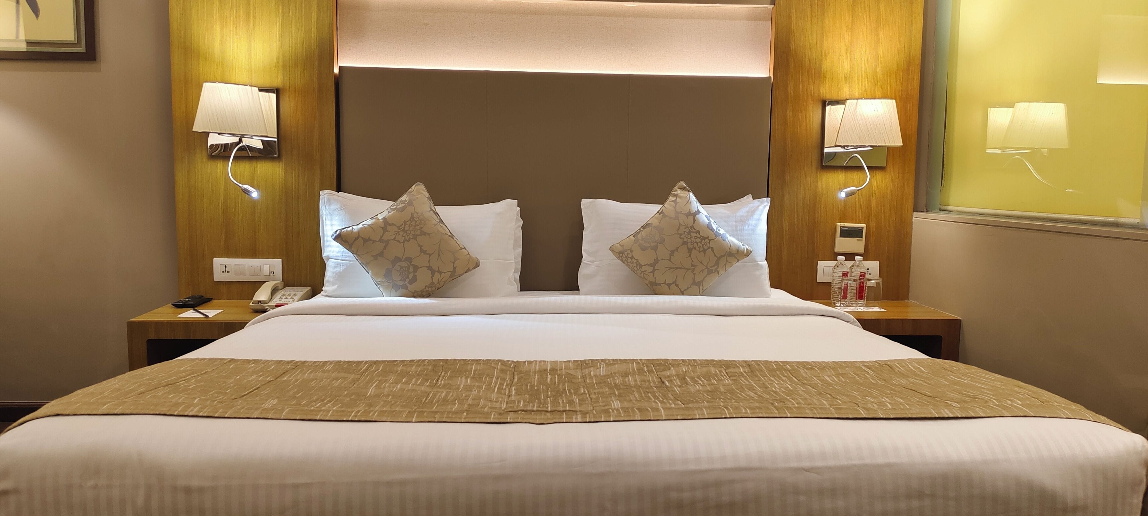 A hotel room with a large bed, two nightstands, a bedside lamp, a telephone, and a bottle of water on the nightstand.