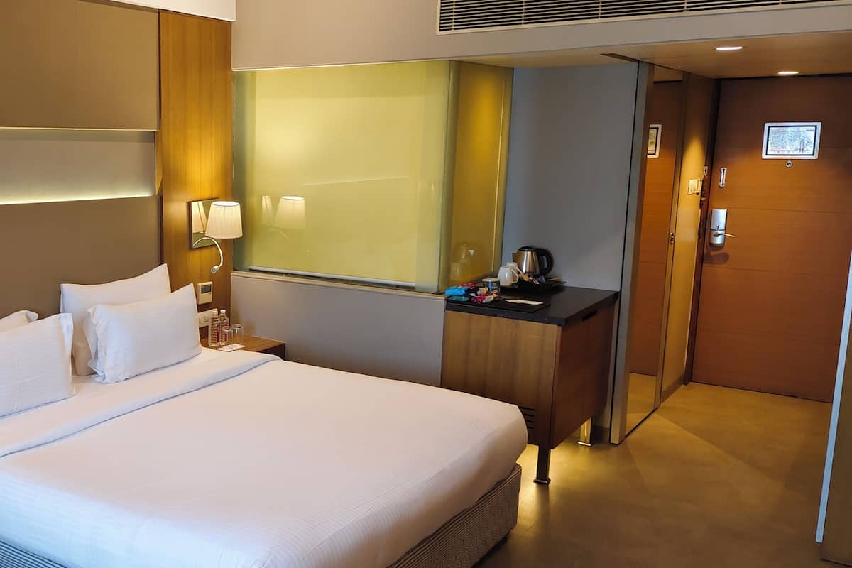 Een hotelkamer met een groot bed, bedlampjes, een nachtkastje, een spiegel en een houten garderobe.