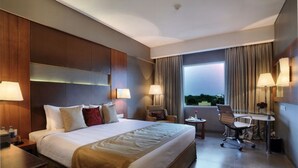 Habitación de hotel con una cama grande, dos mesitas de noche, un escritorio con silla y vistas al exterior.