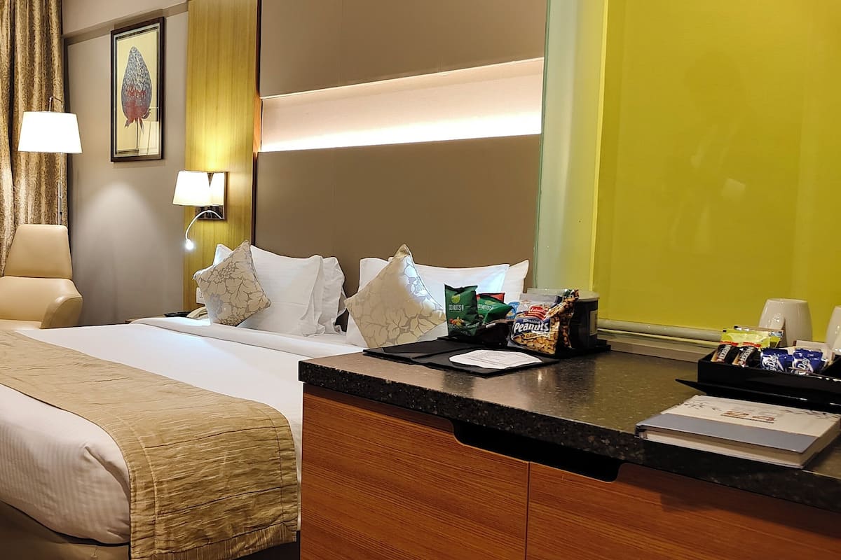 Een hotelkamer met een bed, bureau, stoel, lamp en een schilderij aan de muur.