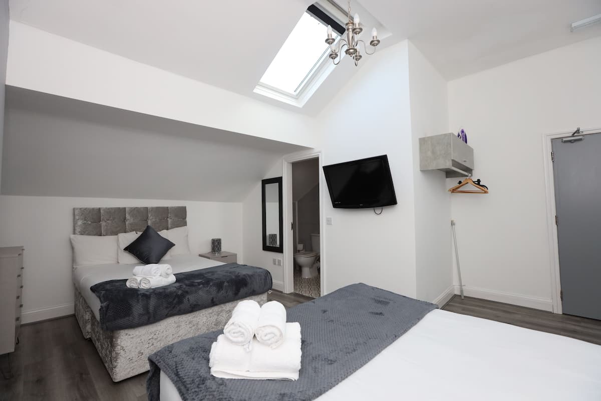 Une chambre moderne avec une lucarne, un lit agrémenté de serviettes roulées, une table de chevet, un téléviseur fixé au mur et une armoire.