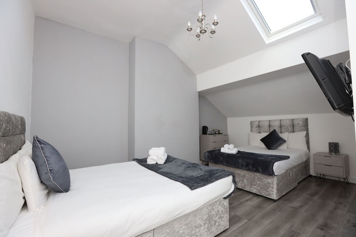 A bedroom with two beds, a chandelier, a desk, and a window.