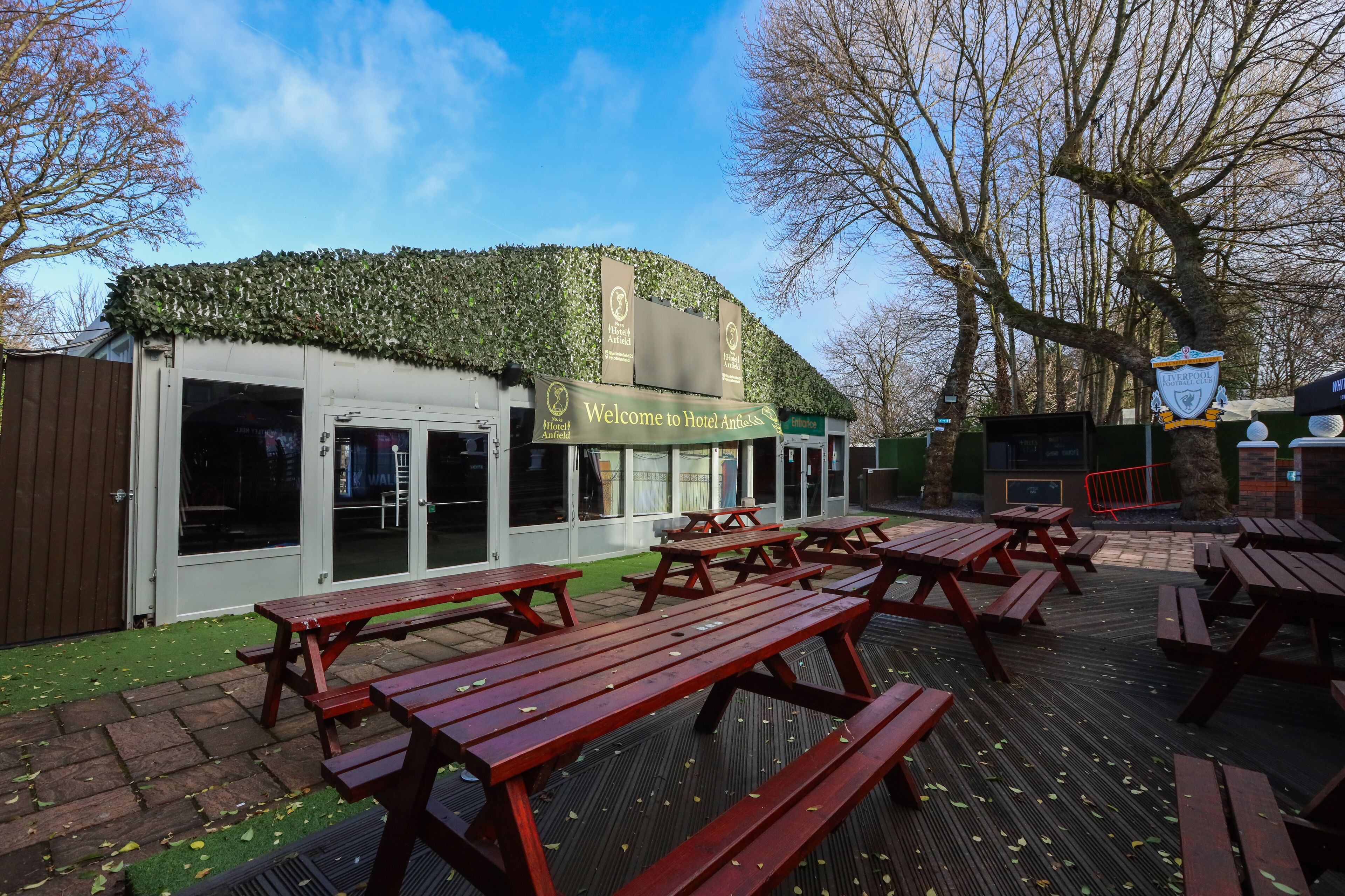 A hotel with a green roof, outdoor seating area with wooden tables and benches, and a sign welcoming guests.