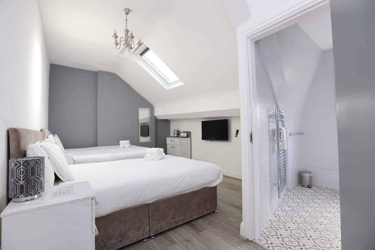 Une chambre moderne avec un grand lit, une table de chevet, une commode, un miroir, un téléviseur à écran plat, une douche et un sol à motifs.