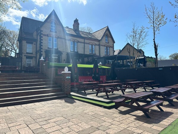 A building with a brick facade, large windows, and a green awning. There are outdoor picnic tables and a staircase leading to the entrance. - Hotel Anfield (Liverpool)
