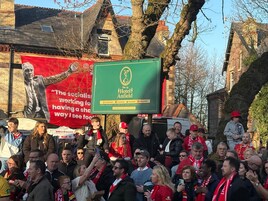 A crowd of people at a hotel event, with a prominent Hotel Anfield sign and a red banner with a political message.
