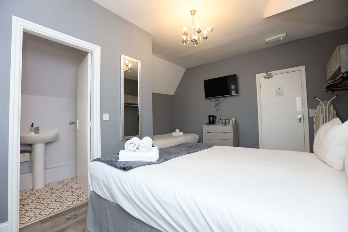 A hotel room with a bed, a bedside table, a mirror, a television, a wardrobe, and a bathroom with a sink.