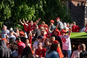 A crowded outdoor event with people in red and white attire, some holding drinks.