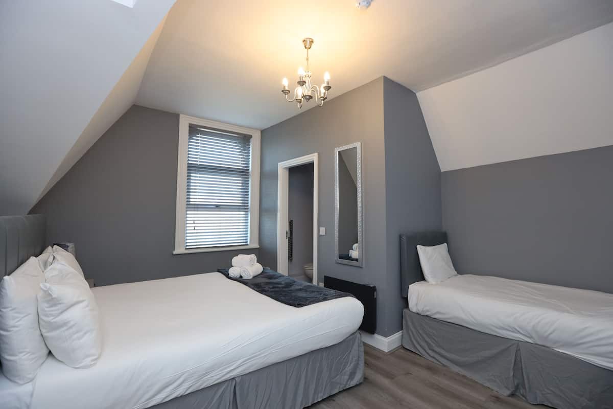 Une chambre avec deux lits, un lustre, une fenêtre avec des stores et un miroir.