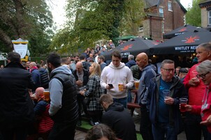 A crowded outdoor event with people standing and socializing, some holding drinks.