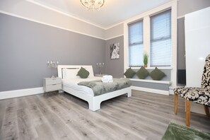 A bedroom with a bed, bedside tables, a window with blinds, a chair, and a chandelier. - Hotel Anfield (Liverpool)