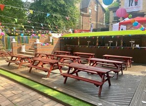 An outdoor patio area with wooden picnic tables and a brick wall. - Hotel Anfield (Liverpool)