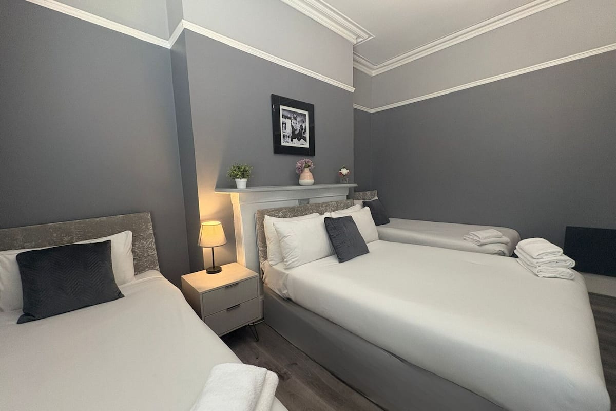 Une chambre d’hôtel avec deux lits, une table de chevet avec une lampe, un tableau encadré au mur et une petite plante en pot.