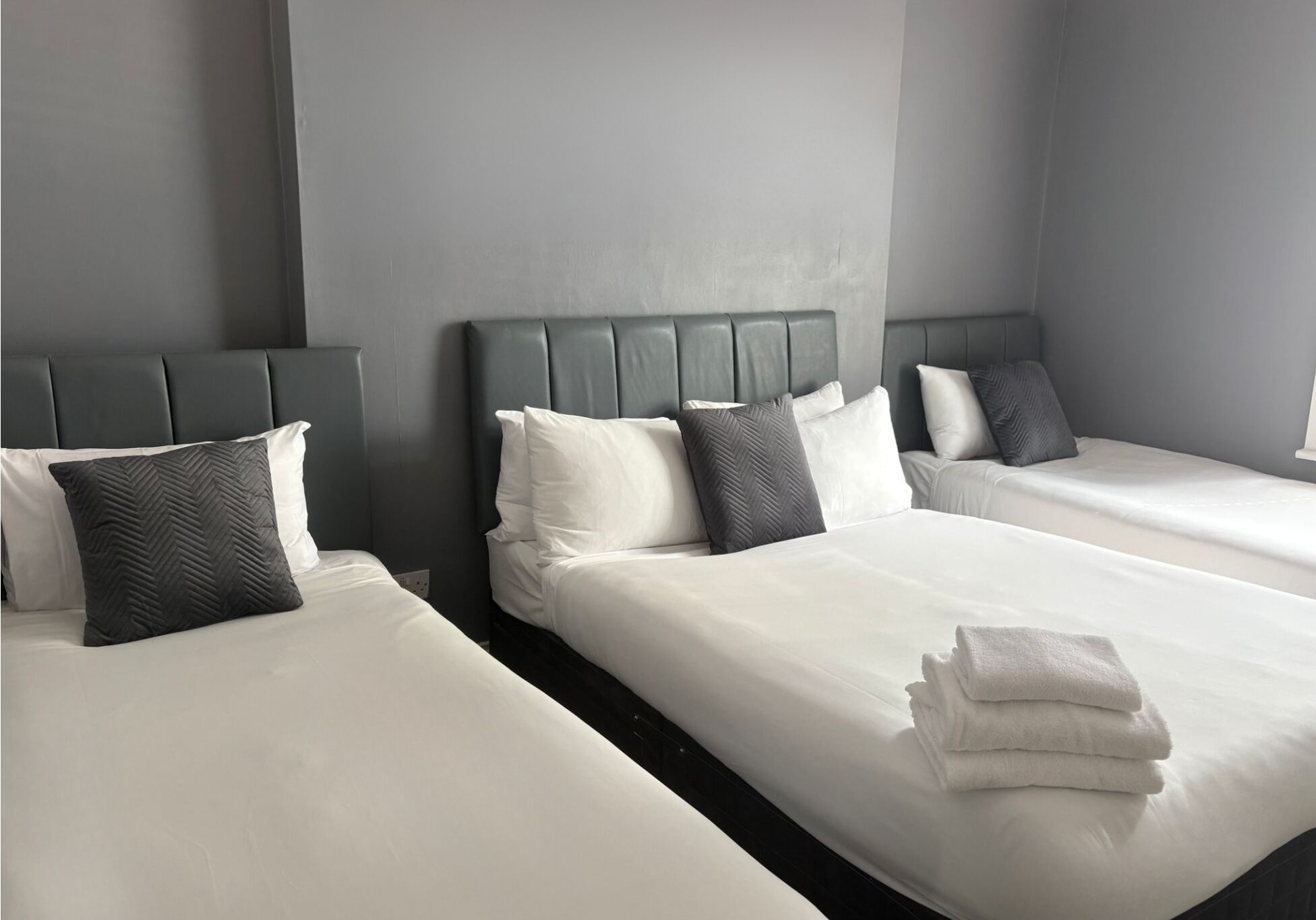 Una habitación de hotel con dos camas, cabeceros grises, ropa de cama blanca y almohadas grises.
