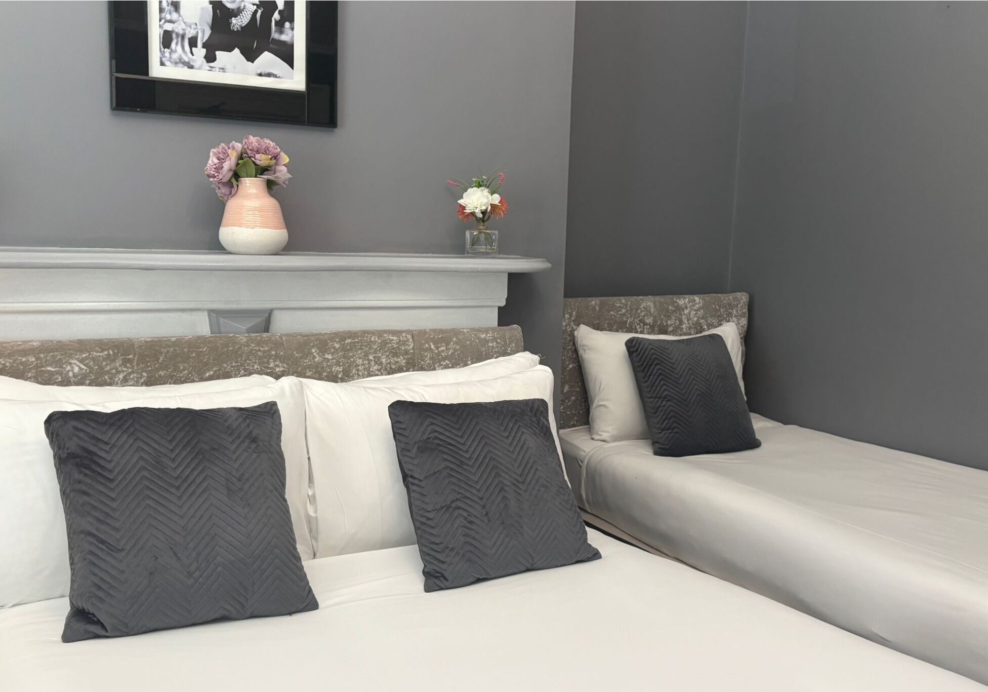 A bedroom with two beds, a white headboard, and a grey wall.