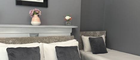 A bedroom with two beds, a white headboard, and a grey wall.