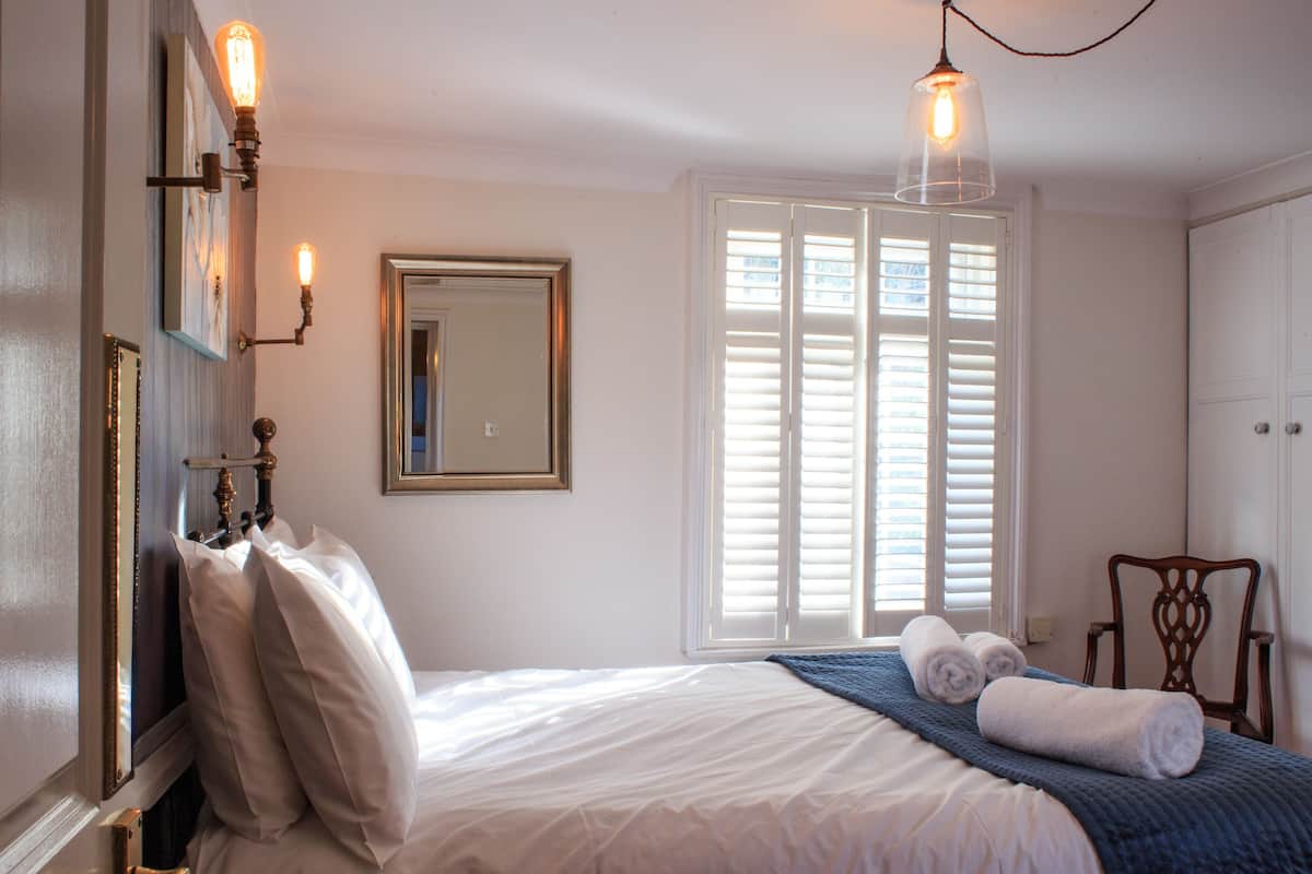 Une chambre à coucher avec un lit, une chaise, une fenêtre avec des volets et des lampes fixées au mur.