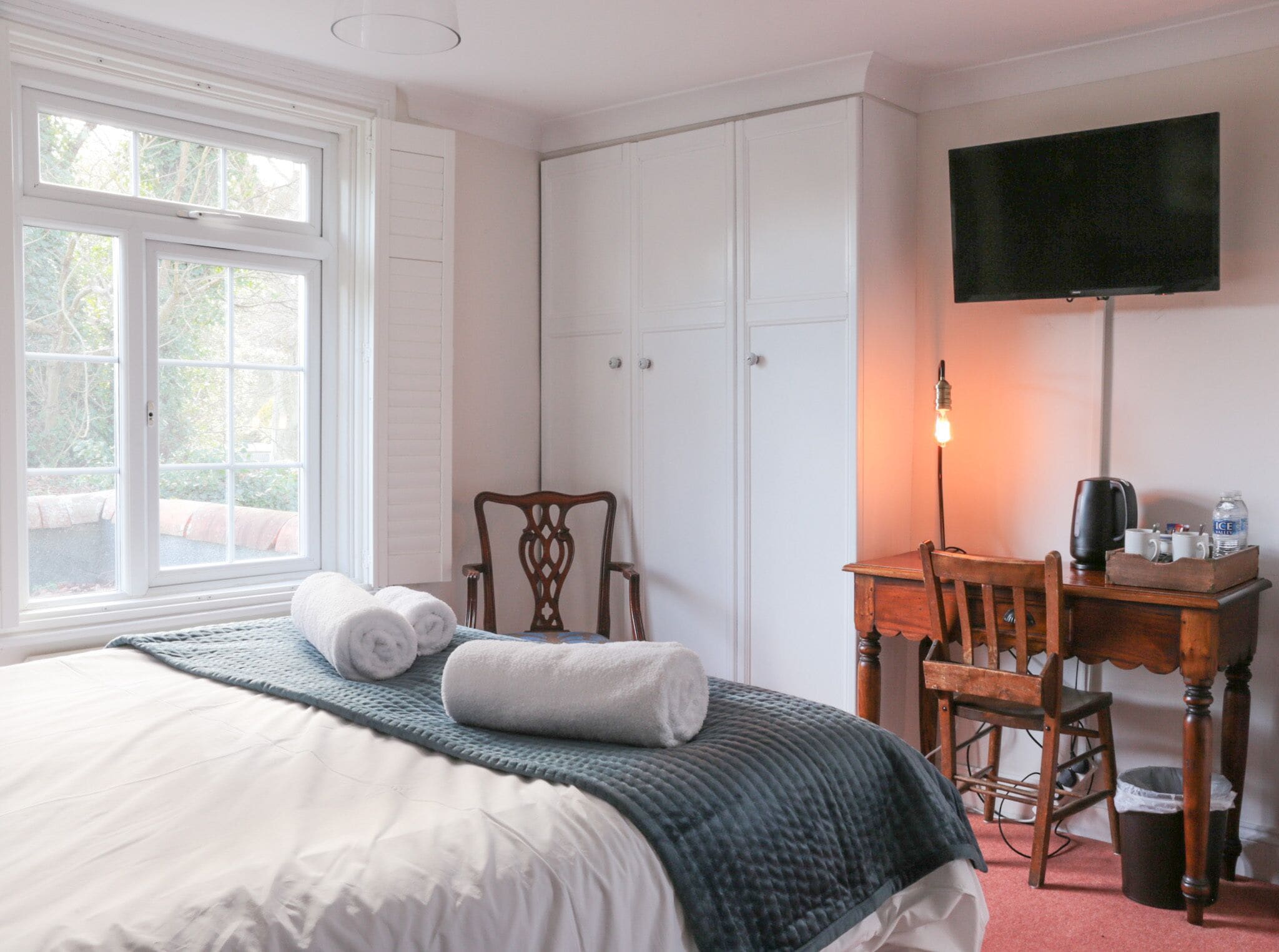 Een slaapkamer met een bed, een bureau, een stoel, een televisie en een raam.