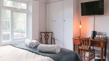 A bedroom with a bed, a desk, a chair, a television, and a window.