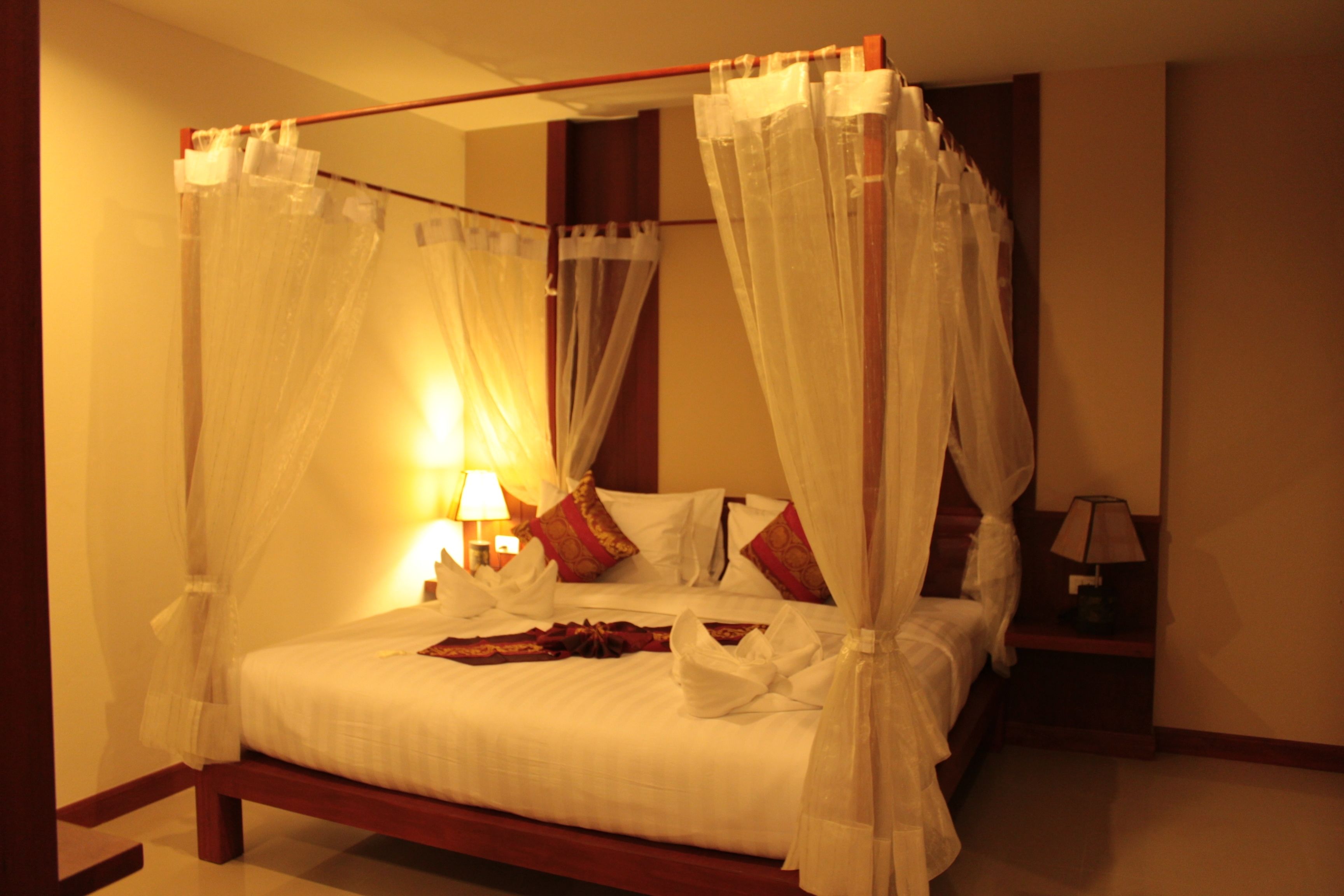 A four-poster canopy bed with white bedding, red pillows, and a bedside table with a lamp.