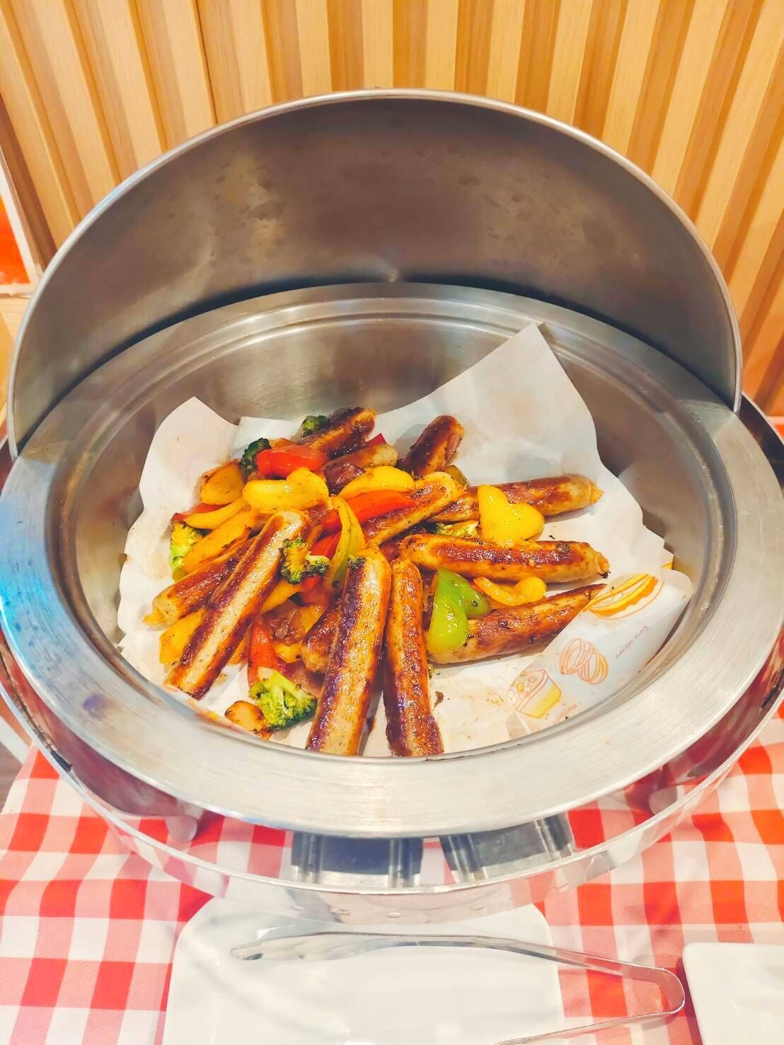 A metal serving dish with food on a checkered tablecloth.
